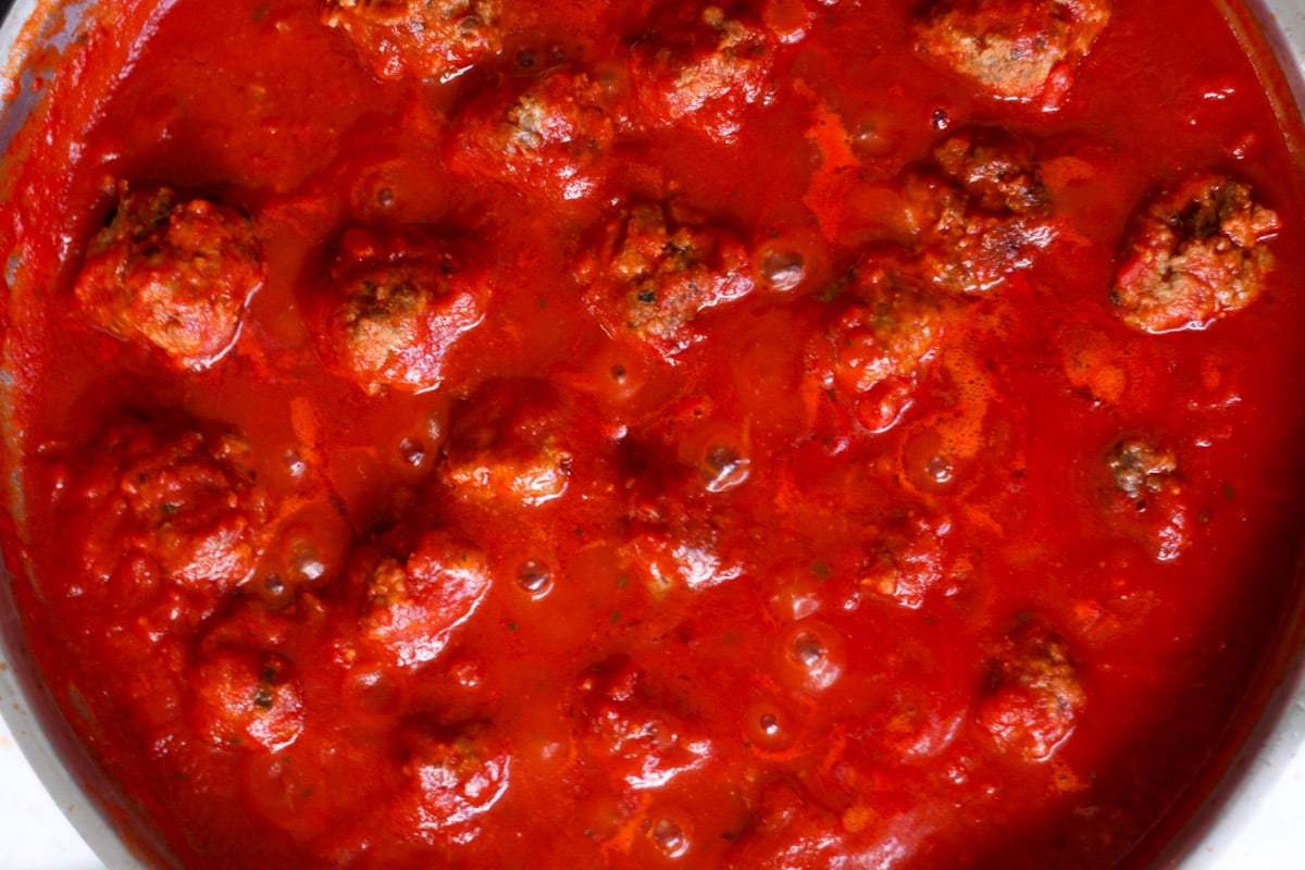 close up image of meatballs cooking in tomato sauce.