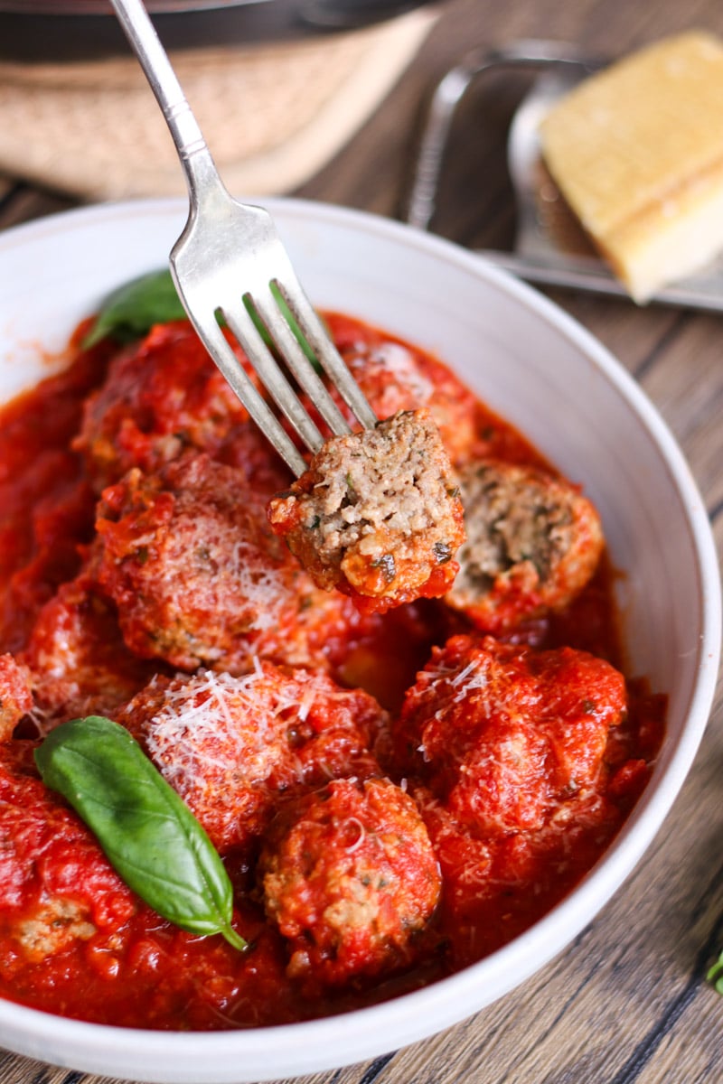 close up image of meatballs on a fork in a white bowl.