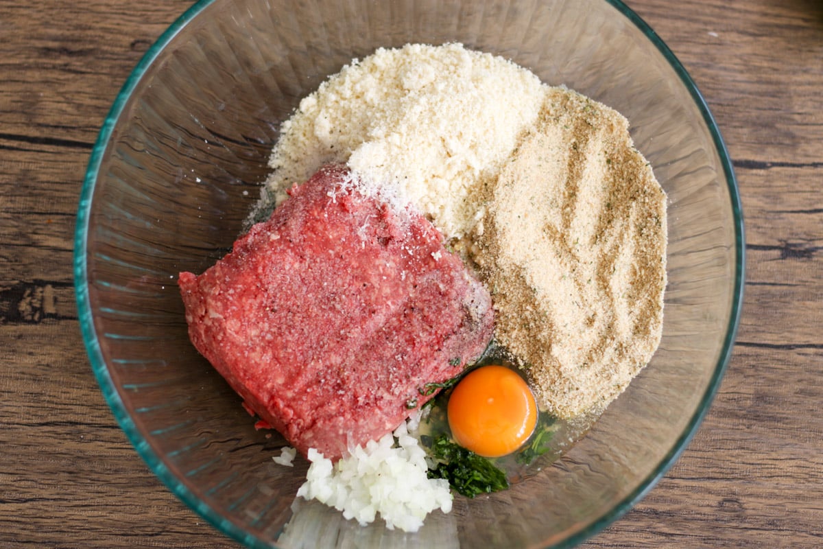 close up photo of ingredients to make meatballs in a glass bowl.