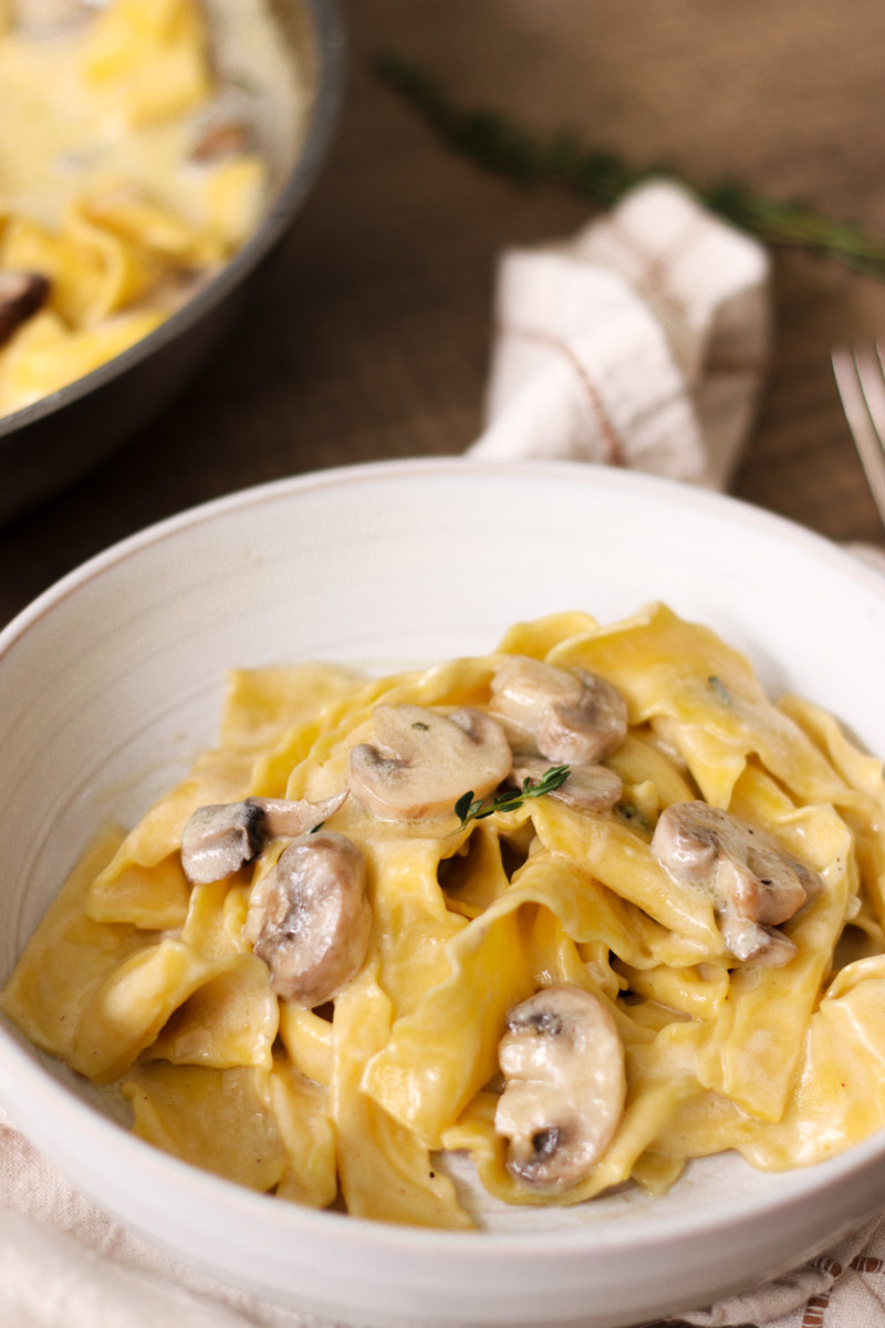 close up image of creamy mushoom pappardelle in a white bowl.