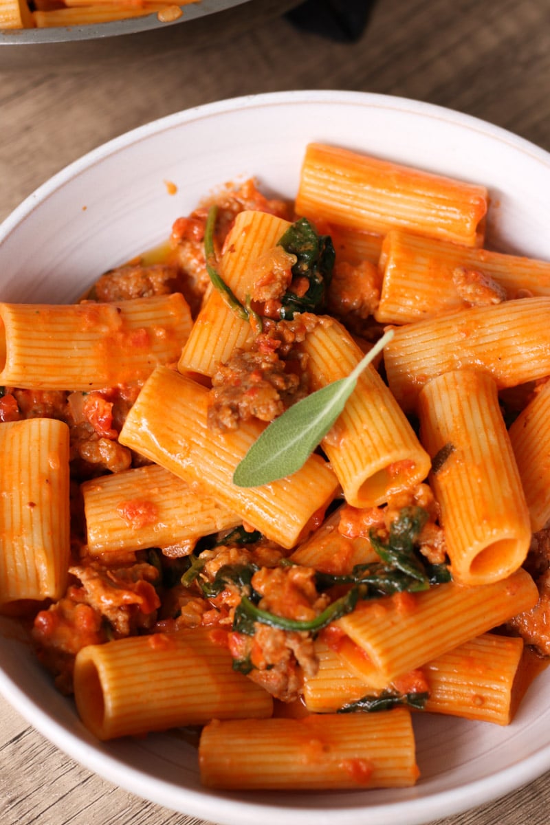 close up image of sausage rigatoni in a white bowl.