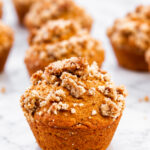 Several streusel-topped pumpkin muffins arranged on a white marble surface.