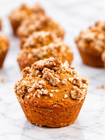 Several streusel-topped pumpkin muffins arranged on a white marble surface.
