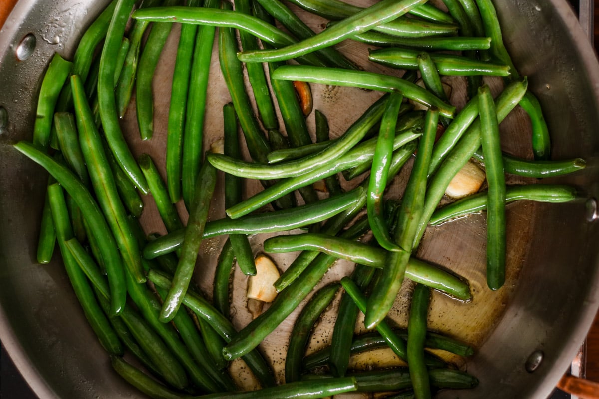 close up image of sauteed greens beans on a white platter.