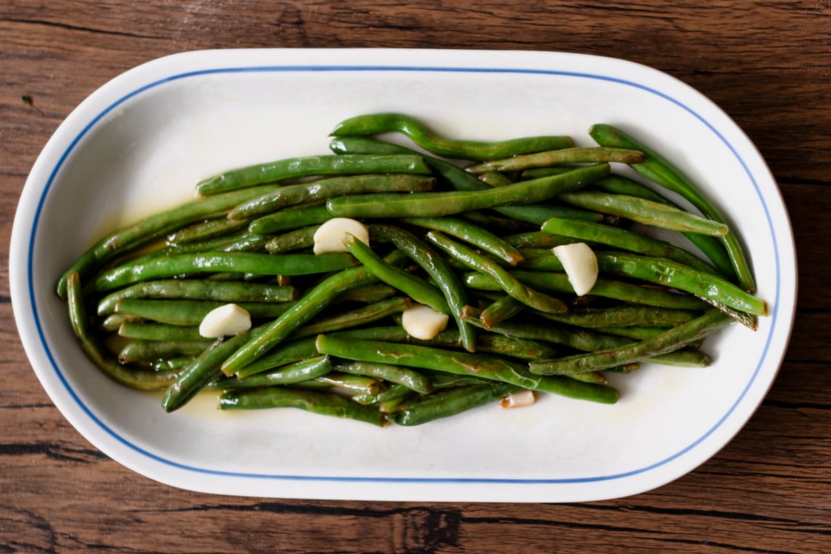Sauteed greens beans on a white platter.