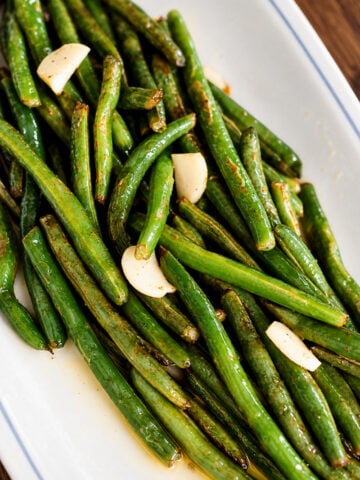 Roasted green beans tossed with garlic cloves on a white platter.