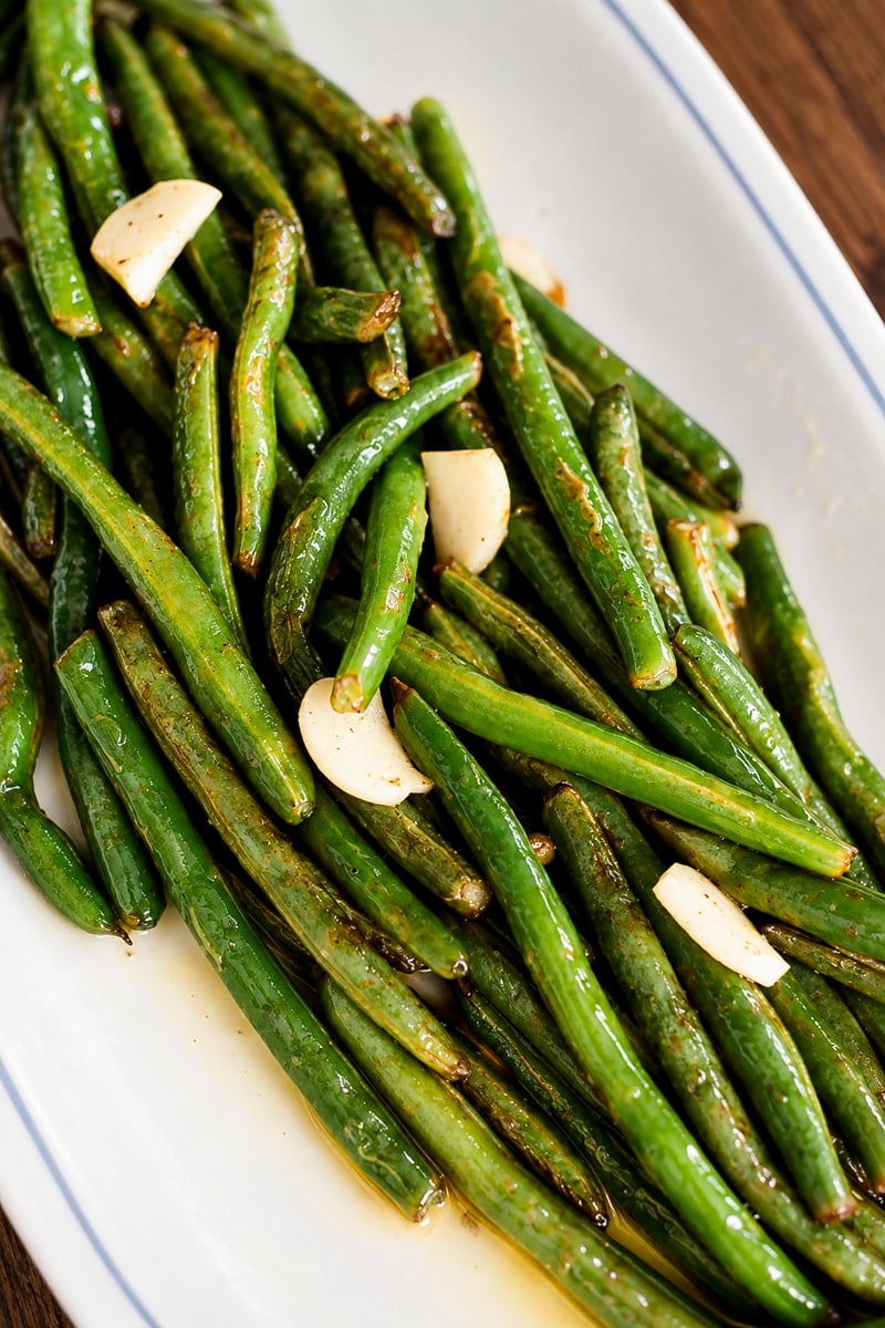 Roasted green beans tossed with garlic cloves on a white platter.