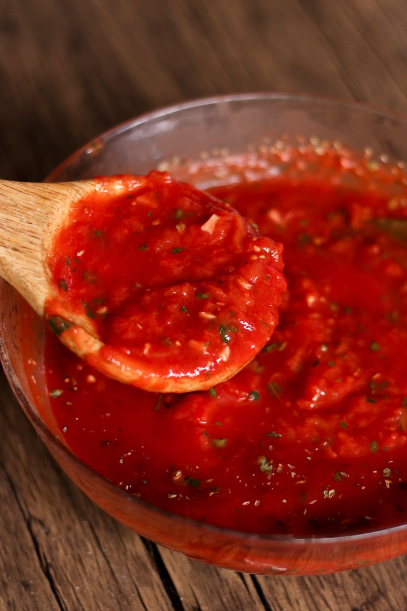 close up image of no cook San Marzano tomato pizza sauce on a wooden spoon.