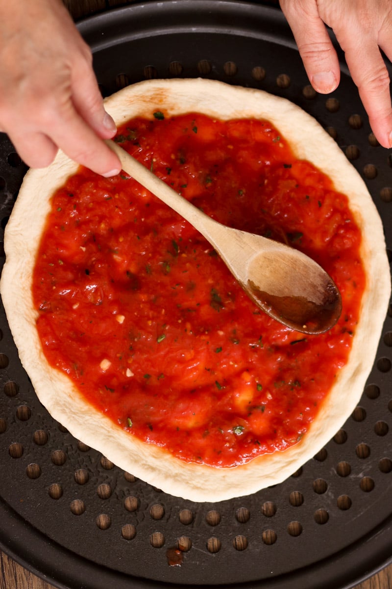 close up image of spreading sauce on pizza.