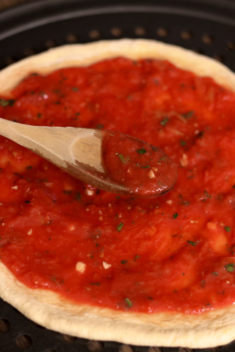 close up image of pizza sauce on a wooden spoon.