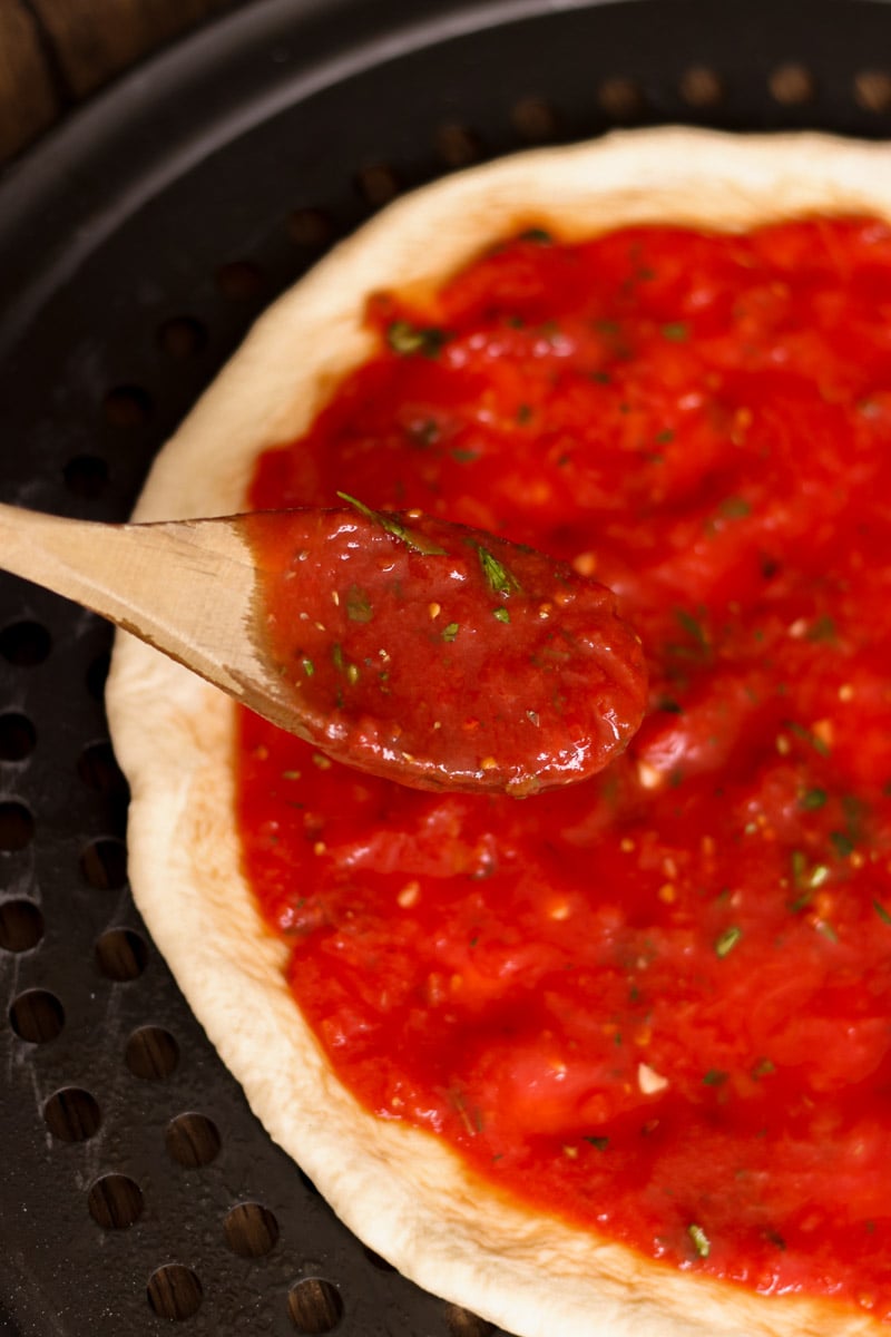 close up image of homemade pizza sauce on a wooden spoon.
