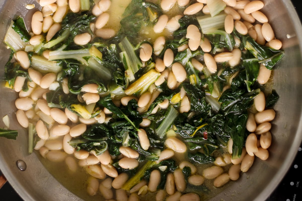overhead image of rainbow chard and white beans in a skillet.
