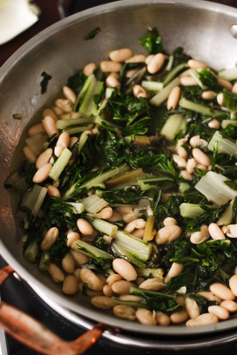 close up image of rainbow chard and beans in a skillet.