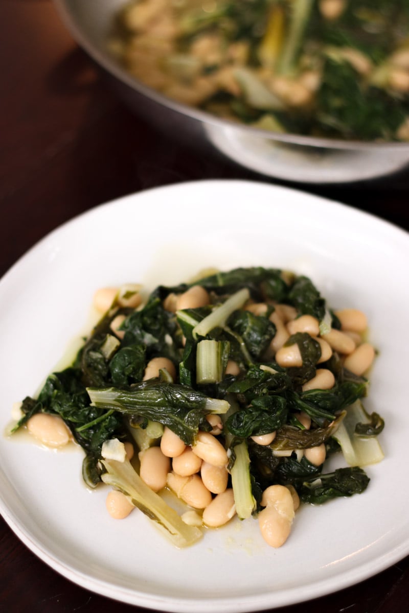 close up image of greens and beans on a white plate.