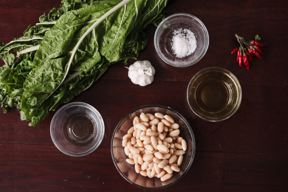 overhead image of ingredients to make rainbow chard and beans on a wooden board.