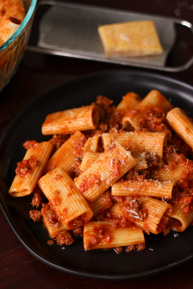 close up image of rigatoni bolognese on a black dish.