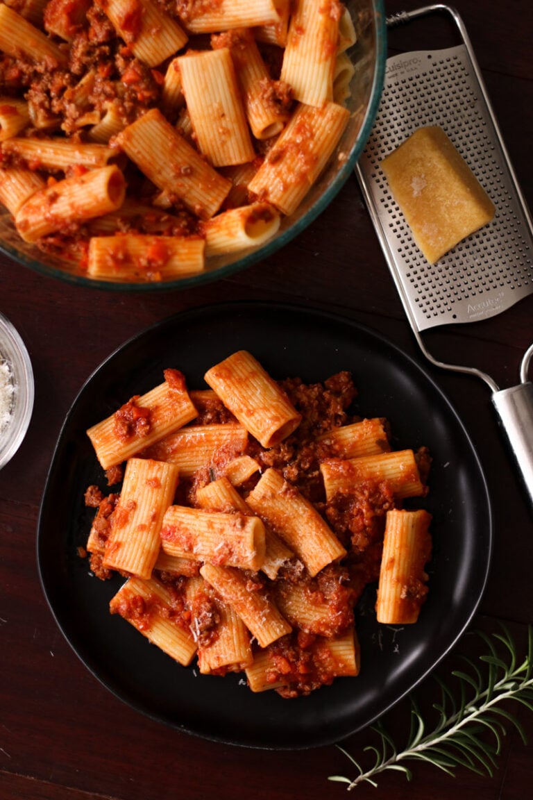 Rigatoni bolognese on a black dish.