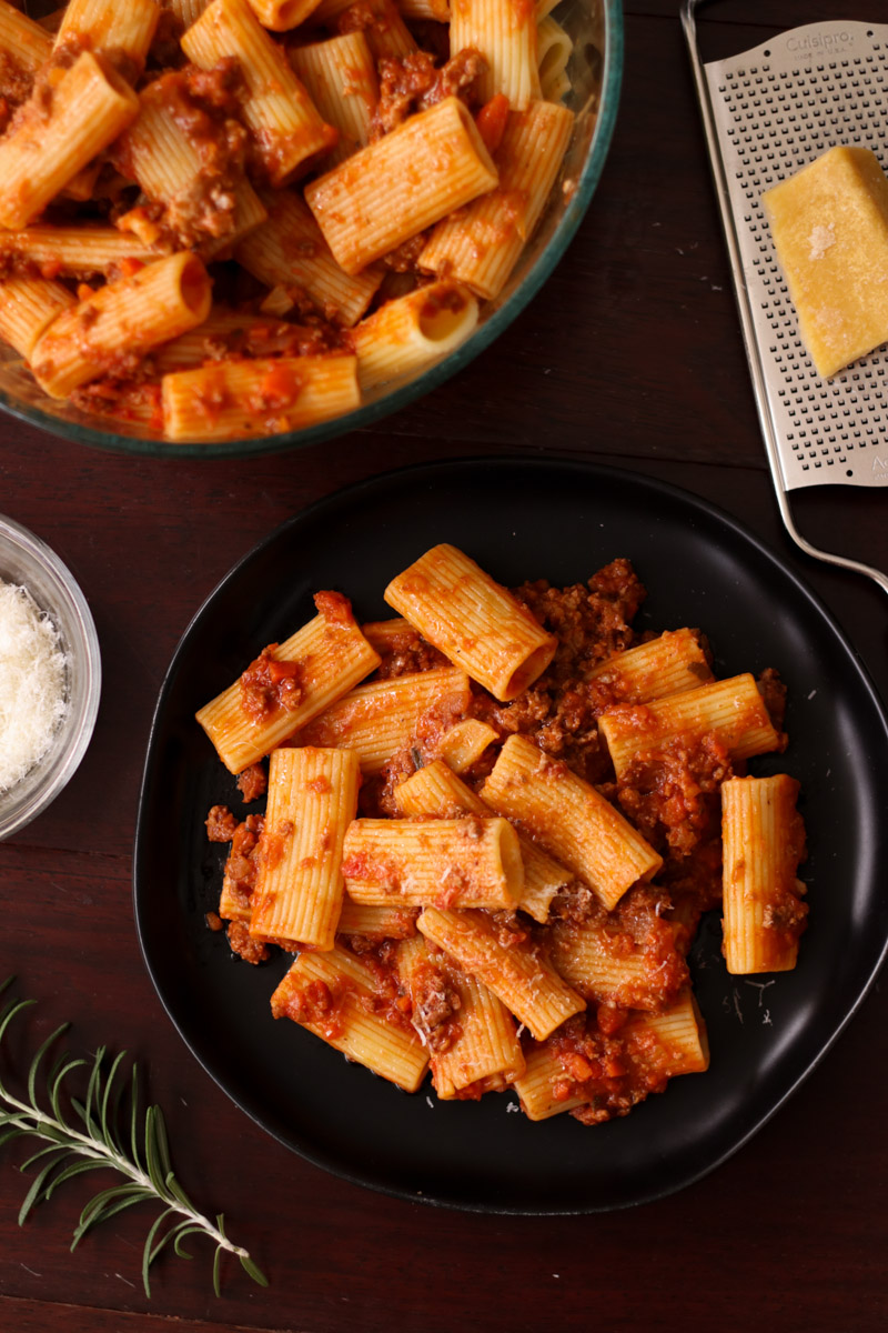 close up image of rigatoni bolognese on a black dish.