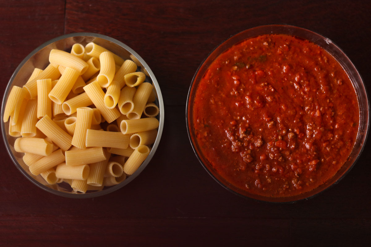 overhead image of pasta and meat sauce in glass bowls. 