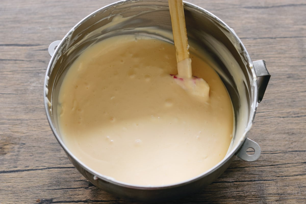close up image of stirring cheesecake filling in a bowl.