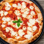 An Easy Homemade Pizza, this Margherita features melted mozzarella cheese, tomato sauce, and fresh basil leaves, served on a black round tray atop a striped woven tablecloth.