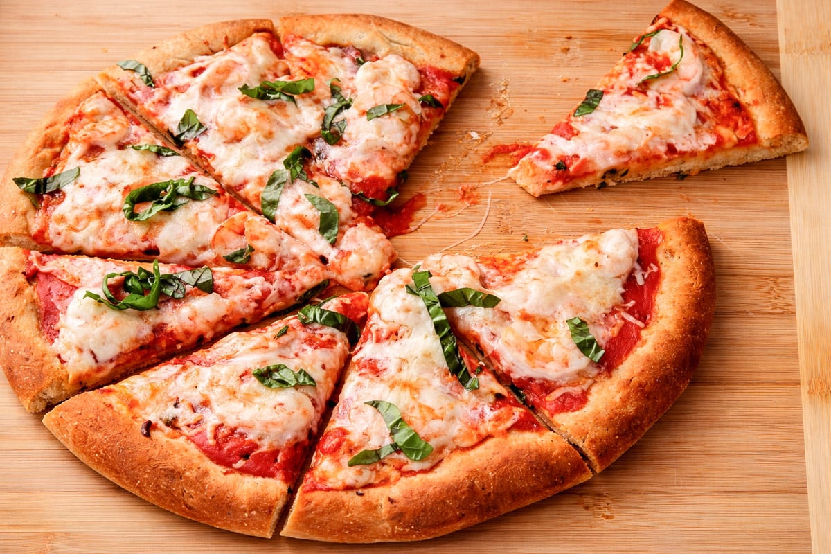 An easy homemade pizza with tomato sauce, fresh basil, and melty cheese sits on a wooden surface, one slice slightly pulled away from the rest.
