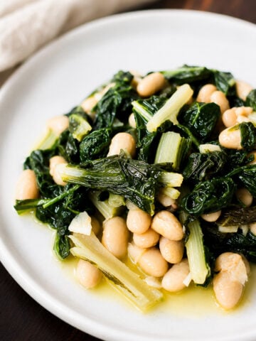 A white plate with saut&eacute;ed rainbow chard and white beans in olive oil, served on a dark wooden table.