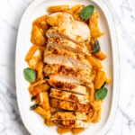 Sliced roasted chicken breast arranged on a white oval platter, surrounded by cooked golden peaches and garnished with fresh sage leaves-much like a classic baked turkey tenderloin presentation-set on a marble surface.