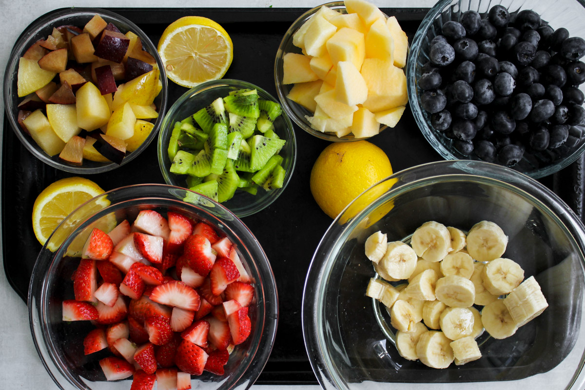 Freshly made Macedonia di Frutta in a glass bowl, combining chopped apples, bananas, kiwis, plums, strawberries, and blueberries, ready to serve.