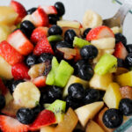 "Close-up of vibrant Macedonia di Frutta showcasing chopped apples, kiwis, plums, strawberries, and blueberries.