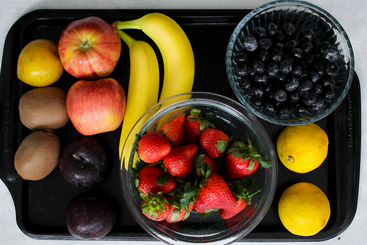 Freshly made Macedonia di Frutta in a glass bowl, combining chopped apples, bananas, kiwis, plums, strawberries, and blueberries, ready to serve.