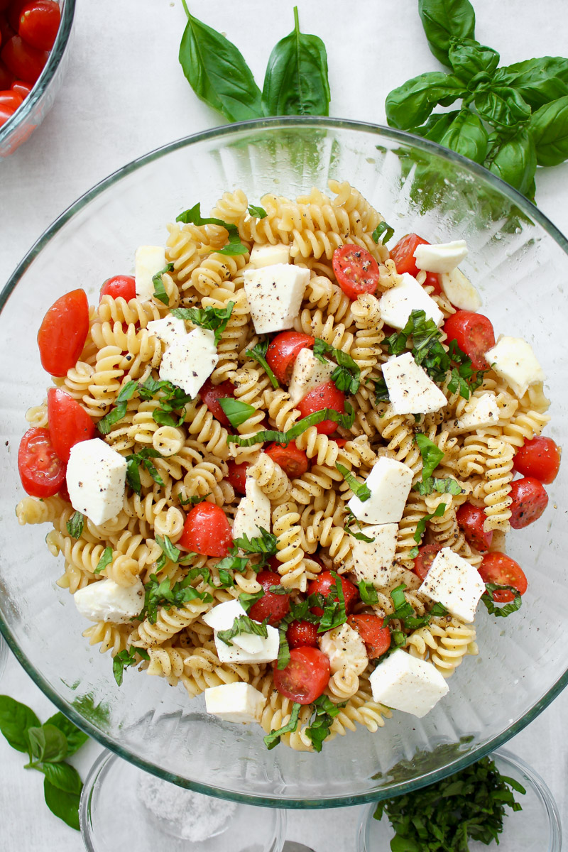 Caprese pasta salad in a glass bowl with cherry tomatoes and basil.