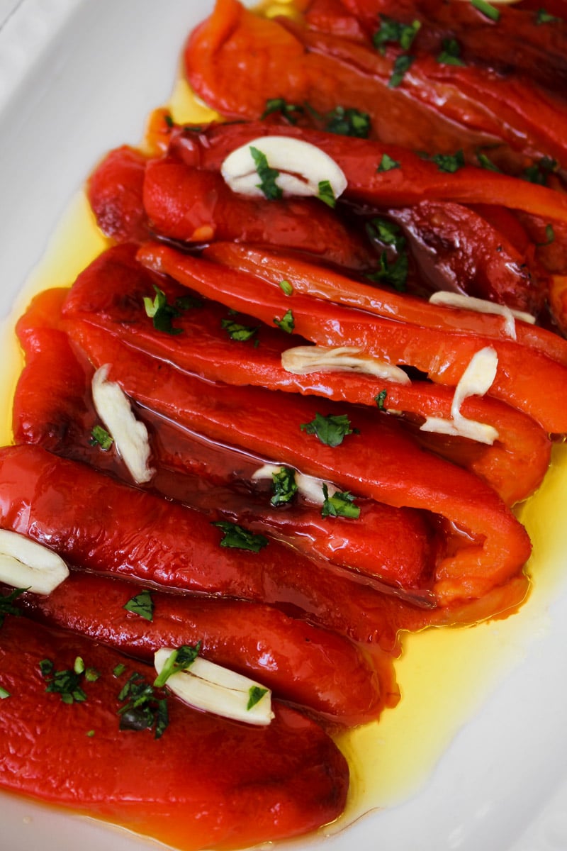 Close-up image of glossy roasted red pepper strips glistening with extra-virgin olive oil.