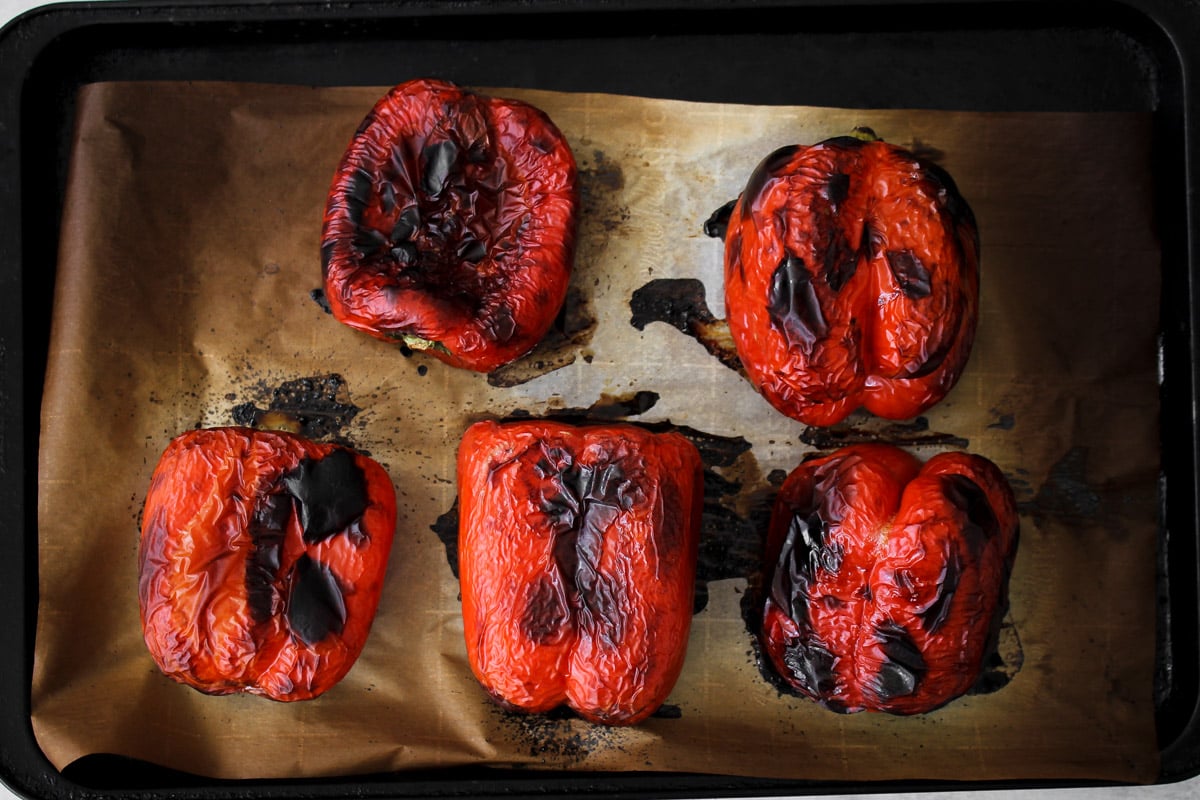 overhead image of whole red bell peppers charred and blistered on a baking sheet fresh from the oven.