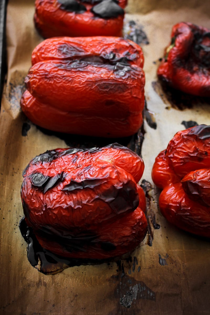 close up shot of charred roasted red peppers on parchment paper ready to be peeled.
