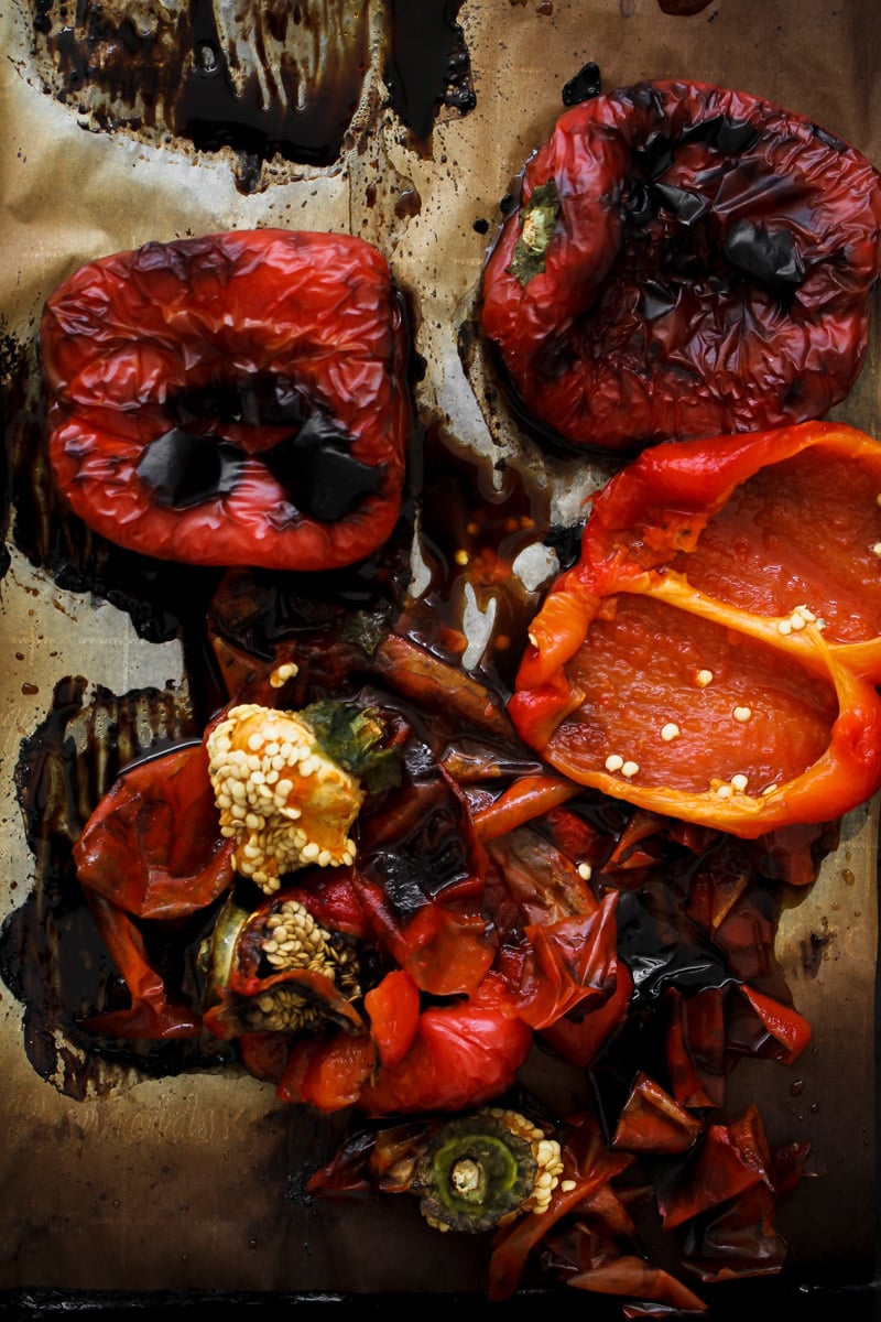 Close up image of whole red bell peppers charred and blistered on a baking sheet fresh from the oven.