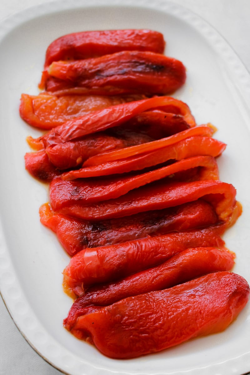 close up image of sliced roasted red peppers arranged on a white dish.