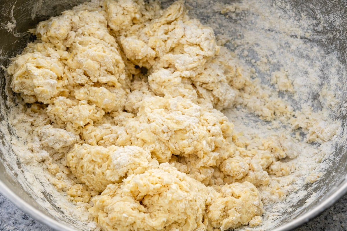 A close-up of raw biscuit dough in a mixing bowl, with visible lumps and a dusting of flour on top&mdash;perfect for starting your favorite Scottish Scones recipe.