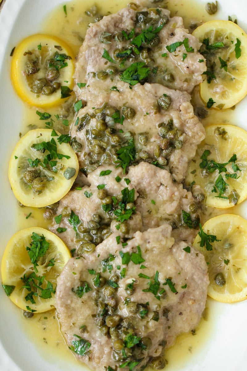 close up image of veal piccata with lemons on a white plate.