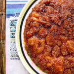 A close-up of a round, caramelized vegan fig upside-down cake with glistening golden-brown fruit topping, served on a white plate with a green and black rim, placed on a striped tablecloth.