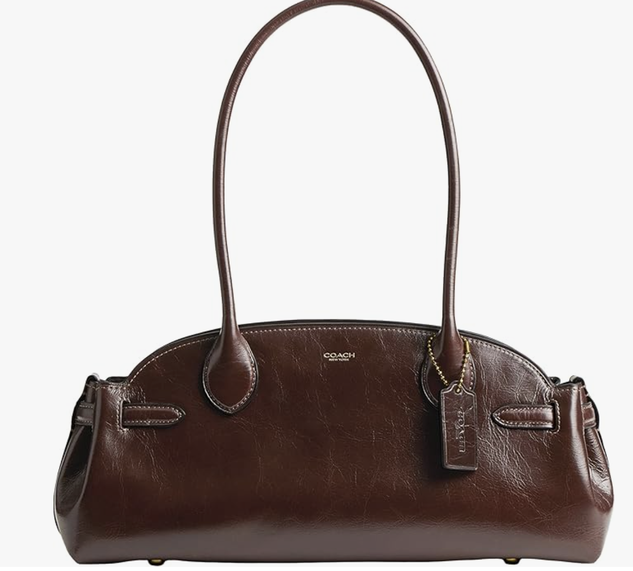 A brown leather Coach handbag with two long handles, gold hardware, and a matching leather Coach tag hanging from one handle, perfect for stylish outings in Italy in December, photographed against a white background.