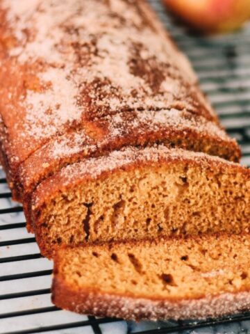 A loaf of cinnamon sugar bread sits on a cooling rack with a couple of slices cut, revealing its moist, golden-brown interior and a dusting of cinnamon sugar-perfect for fans of Apple Cider Donut Cake flavors.