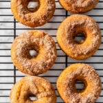 Six cinnamon sugar baked pumpkin spice donuts are arranged in two columns on a black wire cooling rack, placed over a white marble surface.