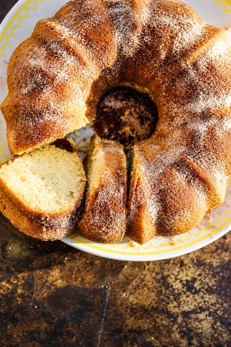 A cinnamon-sugar dusted donut bundt cake on a white plate, with two slices cut from the ring.