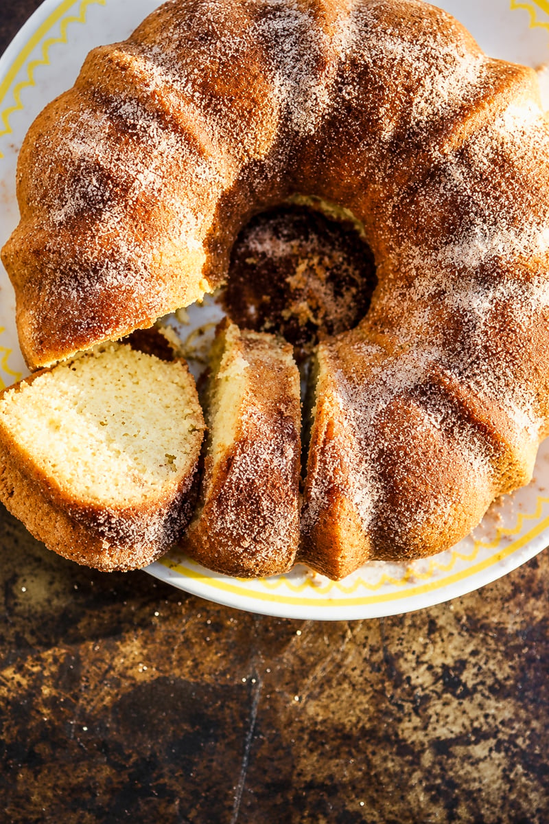 A cinnamon-sugar dusted donut bundt cake on a white plate, with two slices cut from the ring.