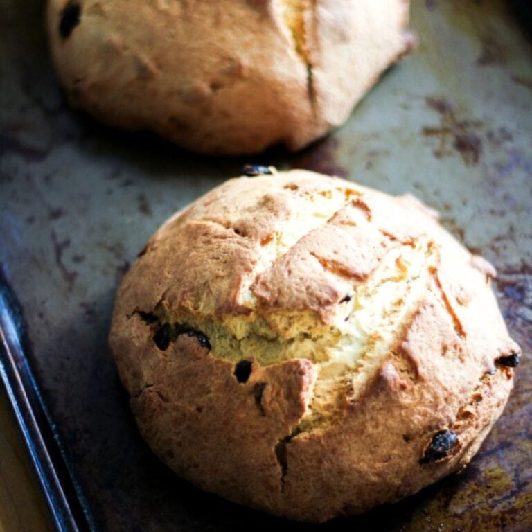 Two round loaves of golden-brown Pandolce Genovese with a rustic, cracked crust and visible raisins, resting on a worn metal baking sheet.