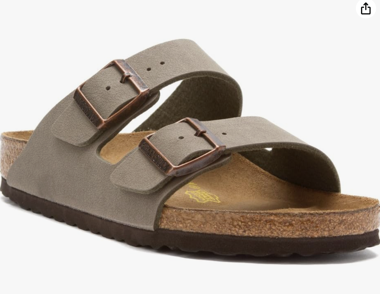 A single sandal with two wide taupe straps, each featuring a copper buckle, a contoured cork footbed, and a dark brown sole-perfect for those planning what to wear in Italy this season.