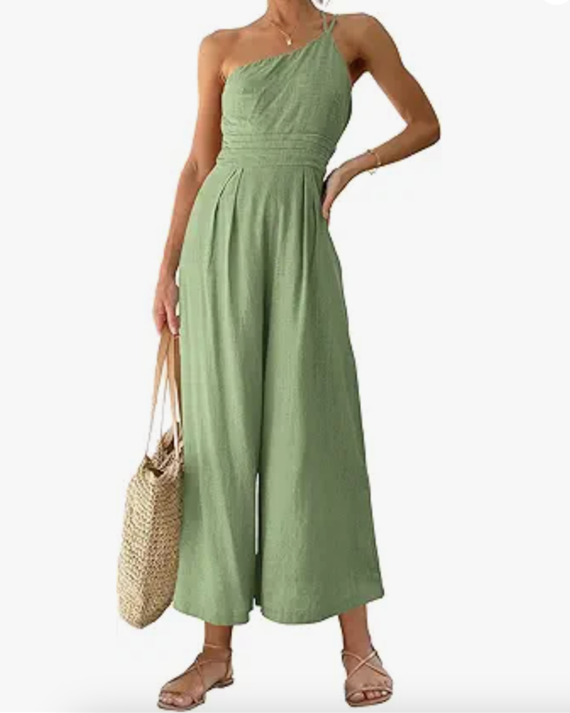A woman wearing a light green, one-shoulder sleeveless jumpsuit with wide legs, holding a straw tote bag and wearing flat sandals-an effortless example of what to wear in Italy for chic, relaxed style.