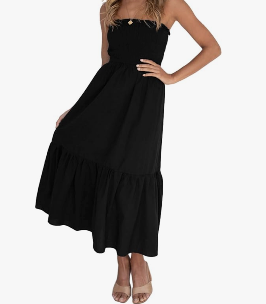 A woman wearing a strapless, black, knee-length dress with a ruffled hem-an ideal choice for what to wear in Italy-stands with one hand on her hip and the other holding the skirt. She is also wearing tan, open-toe heels.
