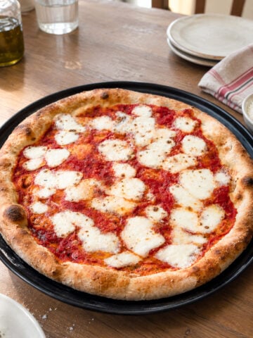 An easy homemade Margherita pizza with tomato sauce and fresh mozzarella on a round black tray, set on a wooden table.